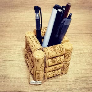 以下が含まれることがあります： リサイクルワインコルクで作られた手作りのペン立て。ペンやマーカーが入っています。コルクには日付とブドウのデザインが刻印されています。ベースには小さな「Handmade」タグが付いています。
