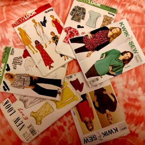 May include: A collection of sewing patterns from New Look and Kwik Sew. The patterns feature illustrations of dresses, tops, and pants. The patterns are on a red and white tie-dye background.