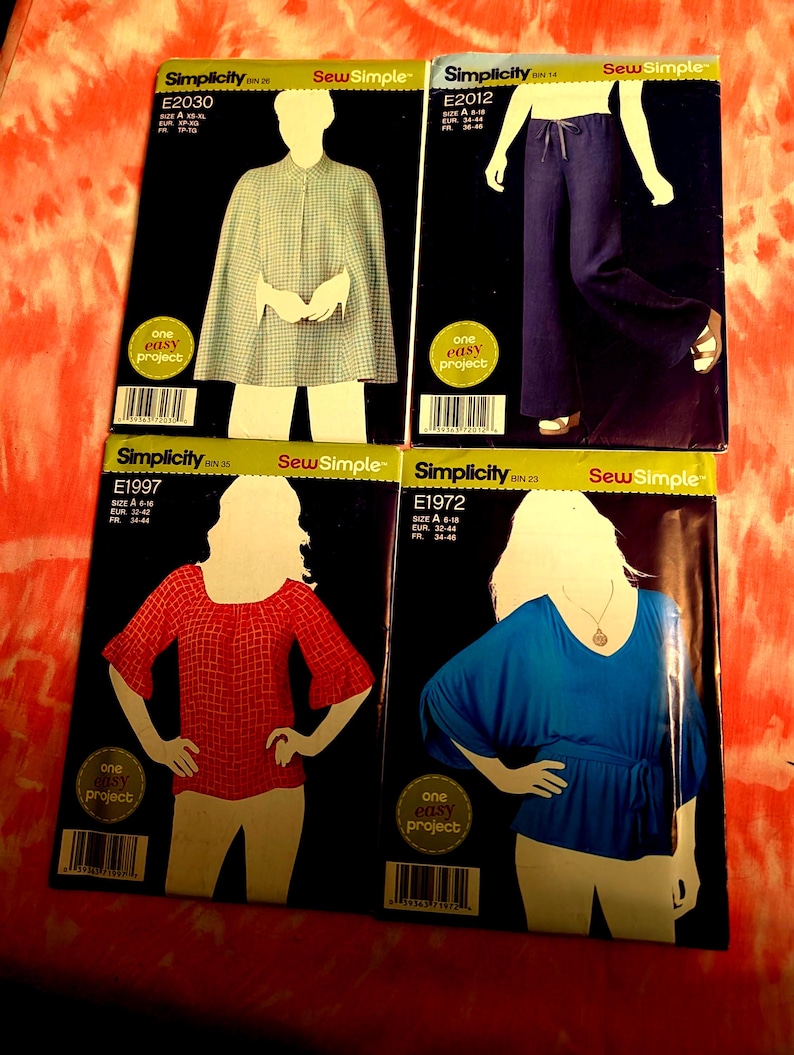 May include: Four Simplicity sewing pattern envelopes. The patterns feature illustrations of a cape, wide-leg pants, a red top, and a blue top. Each envelope has the "Sew Simple" logo and the text "one easy project".