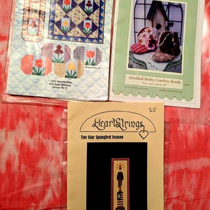 May include: Three craft pattern booklets. "Get Set for Spring" features quilted placemat and wall hanging designs with floral motifs. "Curby's Closet" showcases baby cowboy boots. "HeartStrings" presents a patriotic design, "The Star Spangled Season."