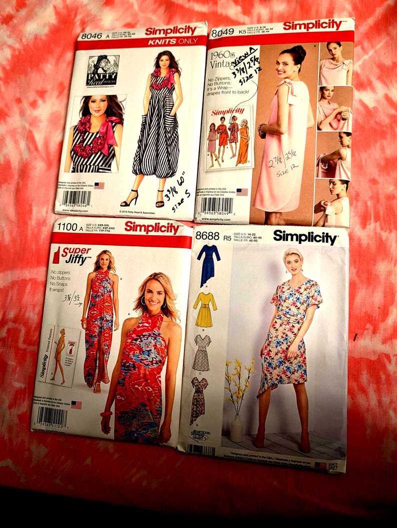 May include: Four Simplicity sewing pattern envelopes. The patterns feature images of dresses and other garments. The envelopes are labeled with numbers and include images of the finished products. The background is a red and white tie-dye fabric.