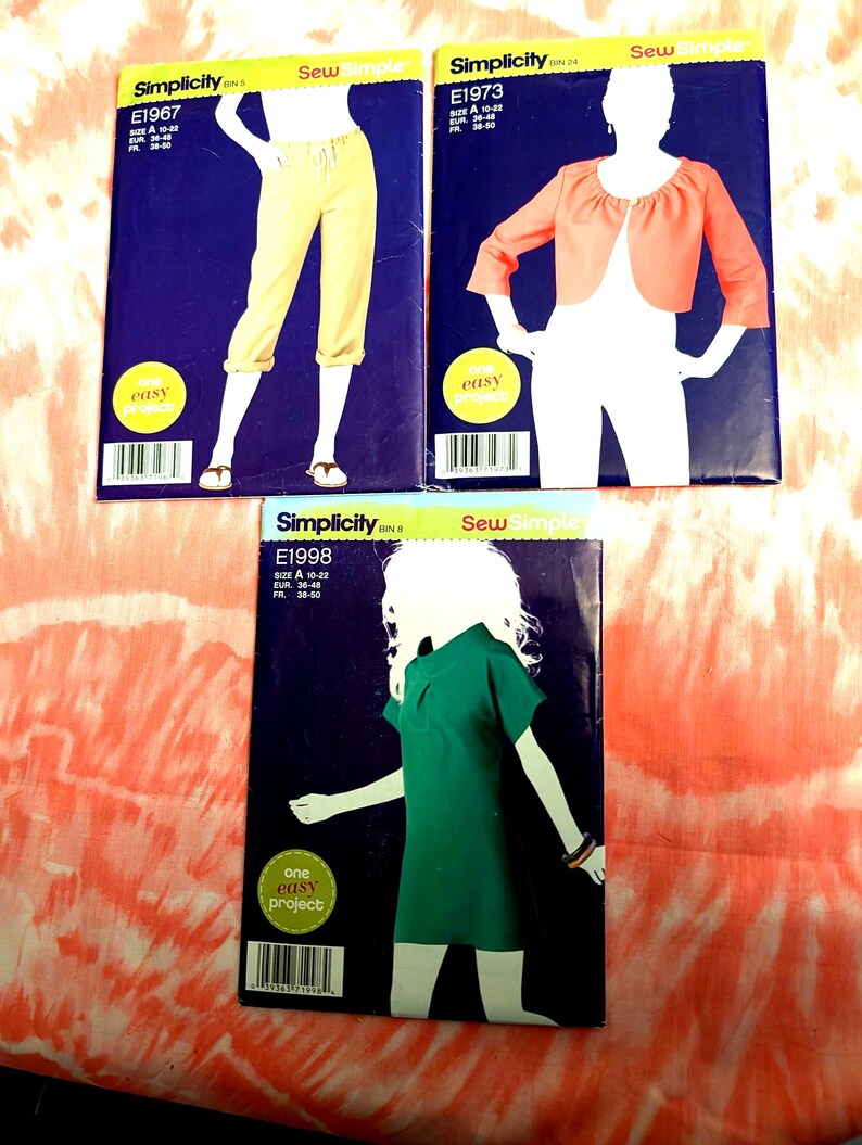 Peut inclure: Trois patrons de couture Simplicity. L'un montre un pantalon capri jaune, un autre une veste bol&eacute;ro corail et le troisi&egrave;me une robe verte. Chaque patron pr&eacute;sente une silhouette et le mot "easy".