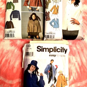 May include: Three Simplicity sewing pattern envelopes. The patterns feature images of jackets, blouses, and capes. The envelopes have the Simplicity logo and text, including size information. The background is a tie-dye pattern.