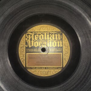 May include: A close-up of a vintage vinyl record with a black label and gold lettering. The label reads "Aeolian Vocalion" and features the song title "Bedouin Love Song" by Wilfred Glenn. The record is in a black sleeve.