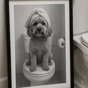 Peut inclure: Photographie en noir et blanc encadrée d'un chien assis sur des toilettes, portant une serviette sur la tête. L'image est prise dans une salle de bain, avec des toilettes et un rouleau de papier toilette en arrière-plan.