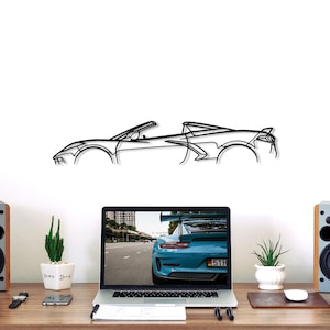 May include: A black metal car outline wall art piece. The artwork is a minimalist depiction of a sports car, mounted on a white wall above a desk. The desk has a laptop, speakers, and plants.