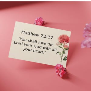 Könnte beinhalten: Eine cremefarbene Karte mit dem Text "Matthew 22:37" und einem Zitat über die Liebe zu Gott. Die Karte ist mit einem floralen Design verziert und von rosa Blumen umgeben, vor einem rosa Hintergrund.