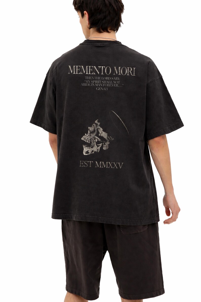 Może przedstawiać: Czarny t-shirt z grafiką i napisem "MEMENTO MORI" oraz wzorem czaszki. Koszulka zawiera r&oacute;wnież tekst "THEN THE LORD SAID, MY SPIRIT SHALL NOT ABIDE IN MAN FOREVER... GEN.6:3" i "EST MMXXV".