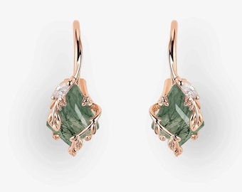 May include: Rose gold earrings with green gemstone pendants. Each earring features a leaf design and a small diamond. The earrings have a hook closure. The background is white.