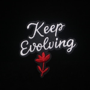 May include: Embroidered patch with the words "Keep Evolving" in white script. A red flower with green stem is below the text. The patch is on a black background.