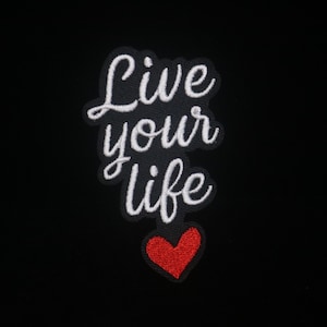 Puede incluir: Parche bordado con las palabras "Live your life" en escritura blanca, sobre un corazón rojo. El parche está sobre un fondo negro. El parche es probablemente para ropa o accesorios.