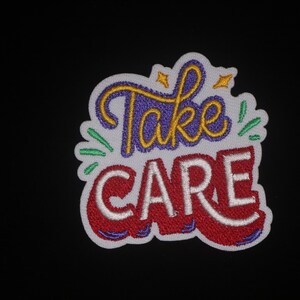 May include: Embroidered patch featuring the words "Take CARE" in a colourful design. "Take" is in purple script with yellow accents, and "CARE" is in red block letters with white outlines. Green and yellow accents surround the text.