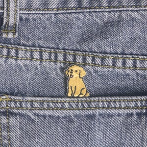 Peut inclure: Un petit écusson brodé en forme de caniche brun clair est cousu sur la poche d'un jean en denim bleu. L'écusson est détaillé avec des contours noirs et est centré sur la poche.