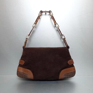 May include: A dark brown suede handbag featuring a structured rectangular body with smooth tan leather accents and embossed crocodile-patterned leather corners. The bag includes a distinctive chain-link handle made of translucent tortoiseshell-style resin.