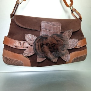 May include: A dark brown suede handbag featuring a horizontal leather strap, crocodile-embossed leather accents, and a central decorative flower made of dark brown fur and crocodile-embossed leather petals, with a brown resin chain link handle.
