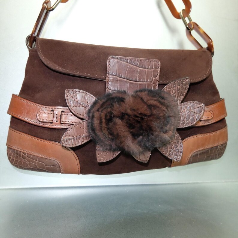 May include: A dark brown suede handbag featuring a horizontal leather strap, crocodile-embossed leather accents, and a central decorative flower made of dark brown fur and crocodile-embossed leather petals, with a brown resin chain link handle.