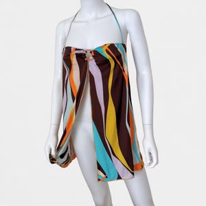 May include: A halter-style top featuring a brown base with vertical wavy stripes in orange, yellow, light blue, and lavender. The garment includes a central circular ring detail at the neckline, connecting the fabric panels in a split-front design.