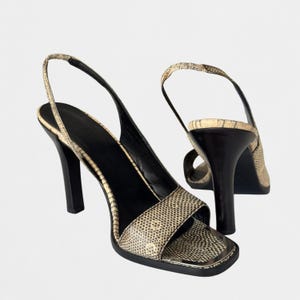 May include: A pair of slingback high-heeled sandals featuring a beige and black snakeskin-patterned texture. The shoes have a square-toe design, a black interior lining, and a solid black heel. The thin heel strap secures the back of the foot.