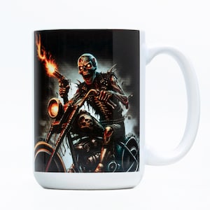 May include: White ceramic mug featuring a detailed illustration of a skeleton riding a motorcycle and holding a flaming gun. The artwork is in shades of black, red, and brown, with a skull on the motorcycle seat. The mug has a white handle and interior.