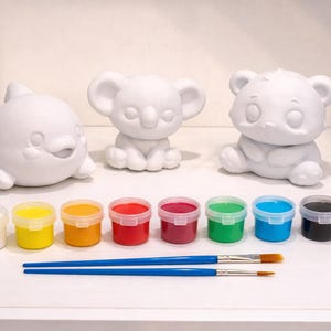 Puede incluir: Kit de manualidades para pintar con tres figuras de cerámica blanca: un delfín, un koala y un oso. Incluye un juego de pinturas de colores en pequeños recipientes y dos pinceles azules. Una actividad creativa.