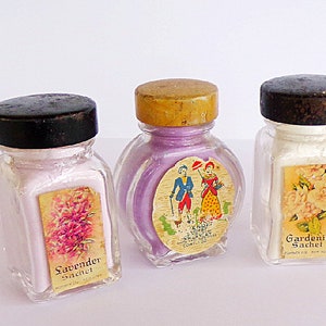 May include: Three small glass jars with black and brown lids. Each jar contains a white powder and has a label with a floral design. The labels read "Lavender Sachet", "Gardenia Sachet", and a label with a couple in period clothing.