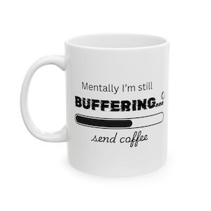 May include: White ceramic coffee mug with the text "Mentally I'm still BUFFERING... send coffee" in black. The mug has a black loading bar graphic. The mug has a white handle.