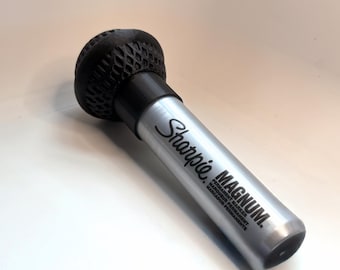 May include: A silver Sharpie Magnum permanent marker with a black textured tip. The marker has the Sharpie logo and the word "MAGNUM" printed on the side. The marker is designed for permanent use.
