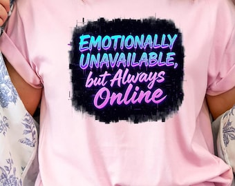 Op de afbeelding: Lichtroze T-shirt met de tekst "Emotionally Unavailable, but Always Online" in neonblauw en roze. De tekst staat op een zwarte, getextureerde achtergrond.
