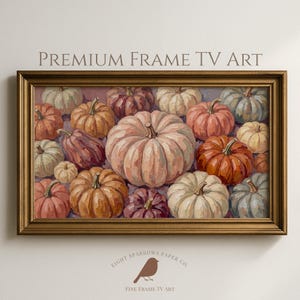 May include: A rectangular wall art piece in a metallic gold frame featuring a painting of numerous pumpkins in shades of orange, cream, muted green, and deep purple. The text "PREMIUM FRAME TV ART" appears above the frame, with a bird logo below.