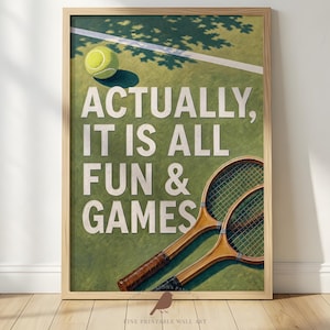 May include: A framed wall art print featuring a green tennis court surface with a white line, a yellow tennis ball, and two wooden tennis rackets. The text reads, ACTUALLY, IT IS ALL FUN & GAMES in large white capital letters centered on the print.