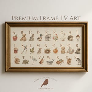 May include: A rectangular wall art piece in a metallic gold frame featuring an alphabet chart with watercolor illustrations for each letter from A to Z, including animals, objects, and nature motifs on a cream background with the text Premium Frame TV Art.