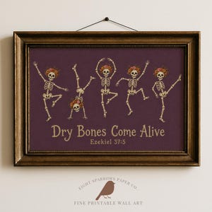 May include: A framed wall art print featuring five skeletons wearing floral crowns in various dancing poses against a dark purple background. The text reads "Dry Bones Come Alive" and "Ezekiel 37:5" in a light tan font. The frame is dark metallic gold.