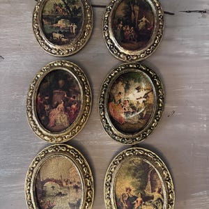 May include: A set of six oval wall plaques featuring ornate gold-colored frames with intricate embossed detailing. Each plaque contains a miniature printed scene depicting historical figures in outdoor settings, including landscapes, garden gatherings, and a canal.