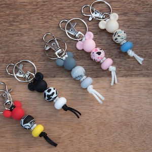 Puede incluir: Seis llaveros coloridos con dijes con forma de Mickey Mouse. Cada llavero presenta un color y un patrón de cuentas diferentes, que incluyen blanco y negro, rojo y negro, gris y blanco, rosa y blanco, y azul y blanco.