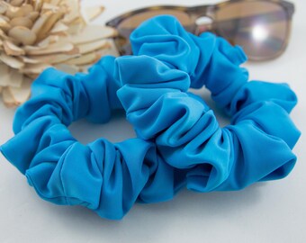 May include: Two bright blue scrunchies made of soft, stretchy fabric. The scrunchies are in a pile, with one on top of the other.