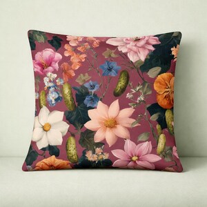 Könnte beinhalten: Quadratisches Kissen mit bordeauxfarbenem Hintergrund und einem Muster aus Blumen und Gurken. Die Blumen sind in Rosa-, Pfirsich-, Weiß- und Blautönen gehalten. Die Gurken sind grün. Das Kissen hat einen dunkelgrünen Rand.