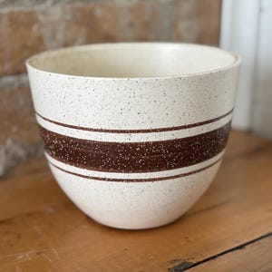 May include: Cream-colored ceramic mixing bowl with brown speckled pattern and two brown stripes. The bowl has a wide, rounded shape and is likely used for food preparation.