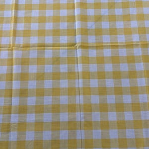 May include: A yellow and white checkered tablecloth. The pattern is a classic gingham design, with evenly spaced squares of yellow and white. The fabric appears to be cotton or a similar material.