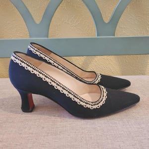 May include: A pair of navy blue pumps with pointed toes and small heels. The shoes have a white, scalloped trim around the opening and a red sole. The heels are approximately 2 inches tall.