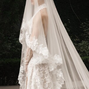 May include: A white lace wedding dress with a high neckline and long veil. The dress features intricate floral lace detailing and a flowing skirt. The veil cascades down the back, creating a romantic and elegant look.