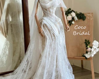 May include: A white lace wedding dress with a sheer veil. The dress features a fitted bodice and a flowing skirt. The text "Coco Bridal" is on a wooden sign.
