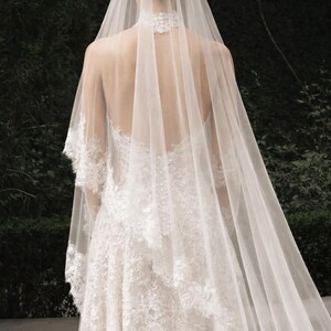 May include: A white lace wedding dress with a long, flowing veil. The dress features intricate lace detailing and a high neckline. The veil cascades down the back, creating an elegant and romantic look.