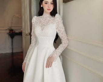 May include: A white wedding dress with a high, lace neckline and long lace sleeves. The bodice features a sweetheart neckline, and the skirt is a flowing A-line. The dress is made of a smooth, satin-like fabric.