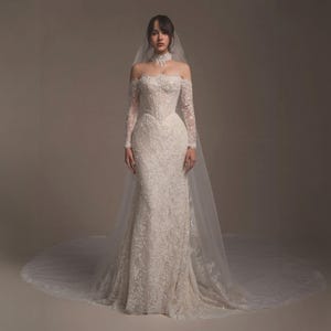 May include: An off-the-shoulder, floor-length ivory wedding dress featuring intricate lace embroidery, long sleeves, and a high-neck lace choker detail. The gown is paired with a long, sheer, floor-sweeping veil that extends beyond the dress hem.