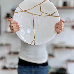 A large white circular platter with gold cracks. The plate is made of ceramic and has a smooth, glossy finish.
