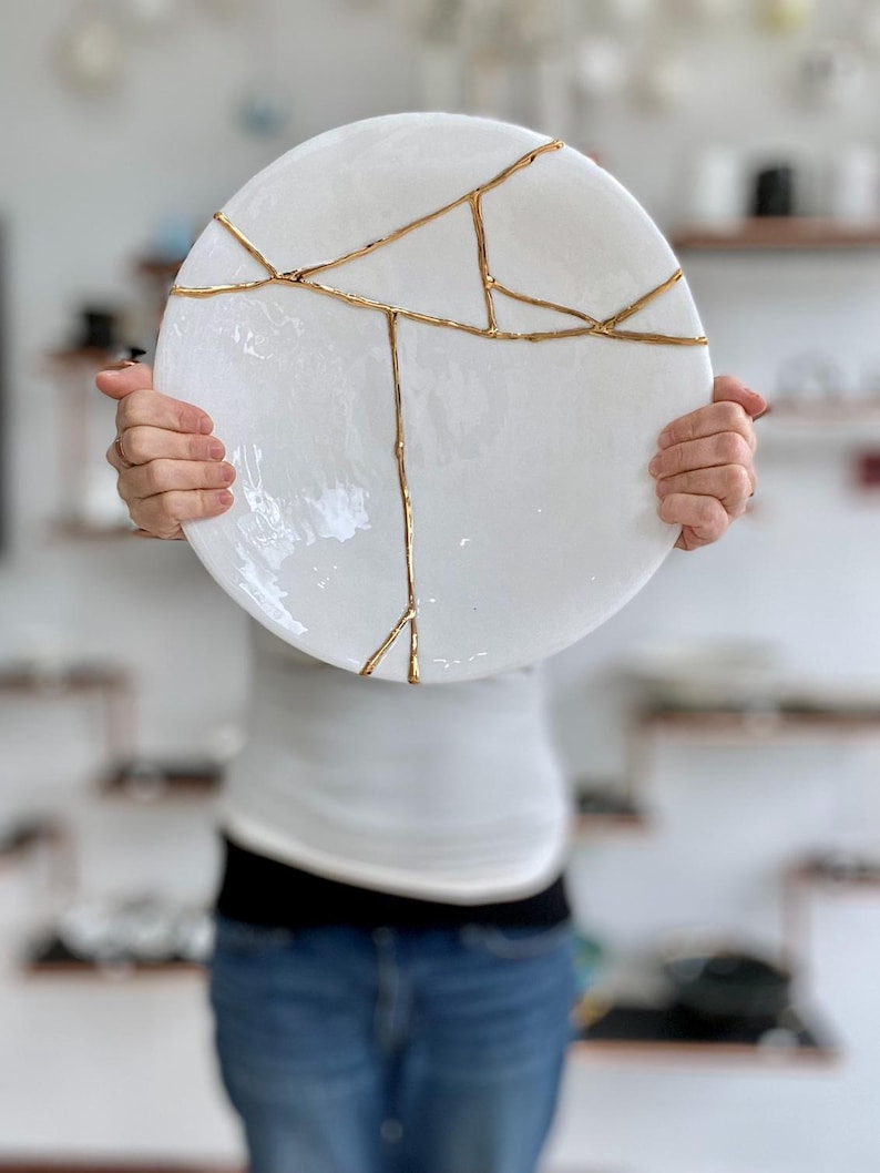 A large white circular platter with gold cracks. The plate is made of ceramic and has a smooth, glossy finish.