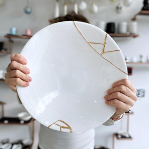 A large white circular platter with gold cracks. The plate is made of ceramic and has a smooth, glossy finish.