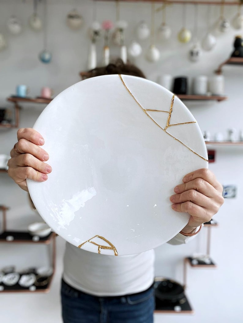 A large white circular platter with gold cracks. The plate is made of ceramic and has a smooth, glossy finish.