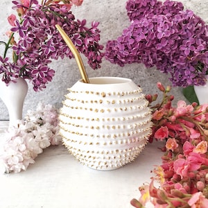 Könnte beinhalten: Weiße Keramik-Mate-Kürbis mit goldenen Stacheln, ein traditionelles südamerikanisches Trinkgefäß, mit einem goldenen Metall-Bombilla-Strohhalm.