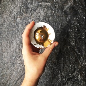 K&ouml;nnte beinhalten: Eine kleine, wei&szlig;e Keramikschale mit goldenem Innenraum. Die Schale hat einen leicht erh&ouml;hten Rand und eine glatte, gl&auml;nzende Oberfl&auml;che.